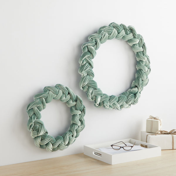sage green wreath in two sizes hanging on a white wall